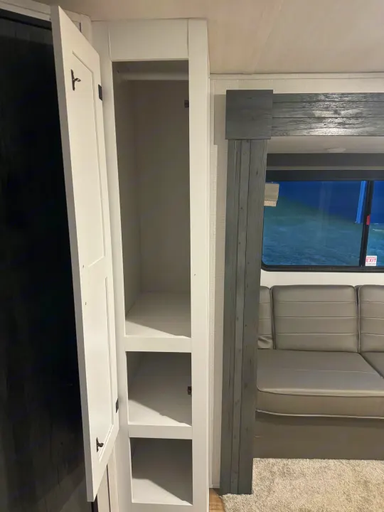 RV rental interior: open white cabinet with storage shelves & hanging rod, plus sofa and window.. keystone hideout 2022
