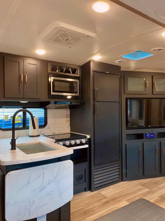 Clean, modern RV rental kitchen & living space: features dark cabinets, full appliances, TV, and skylight.. Keystone RV Outback Ultra-Lite 2022