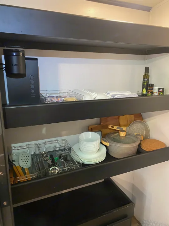 Organized shelves in an RV rental kitchen, featuring a coffee maker, dishes, utensils, cooking essentials, and spices.. Keystone RV Outback Ultra-Lite 2022