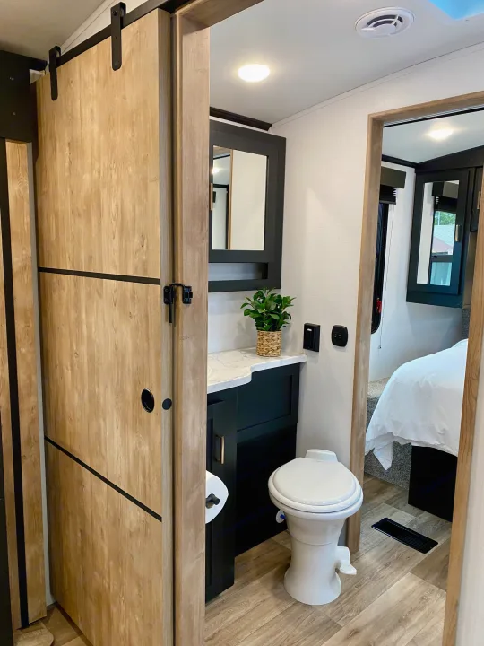 Modern RV rental interior showing a compact bathroom with vanity, toilet, and sliding barn door, leading to the bedroom.. Keystone RV Outback Ultra-Lite 2022