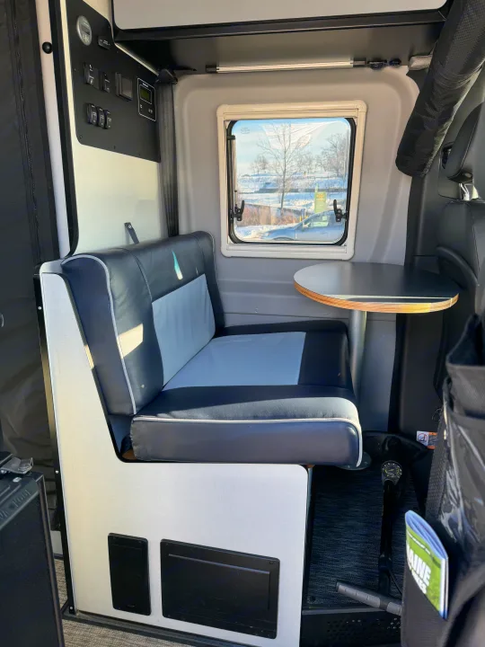 Interior view of an RV rental, featuring a gray dinette bench, table, and a wall-mounted control panel.. Winnebago Revel 2022