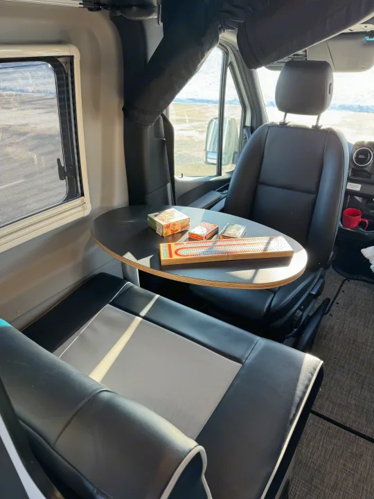 Relaxing in an RV rental: A cribbage board & cards are set on a table between two comfy seats, overlooking outside views.. Winnebago Revel 2022