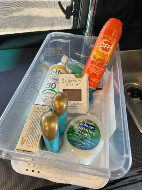 Travel essentials like bug spray, sunscreen, and soap, neatly packed in a bin for an RV rental trip's hygiene needs.. Winnebago Revel 2022