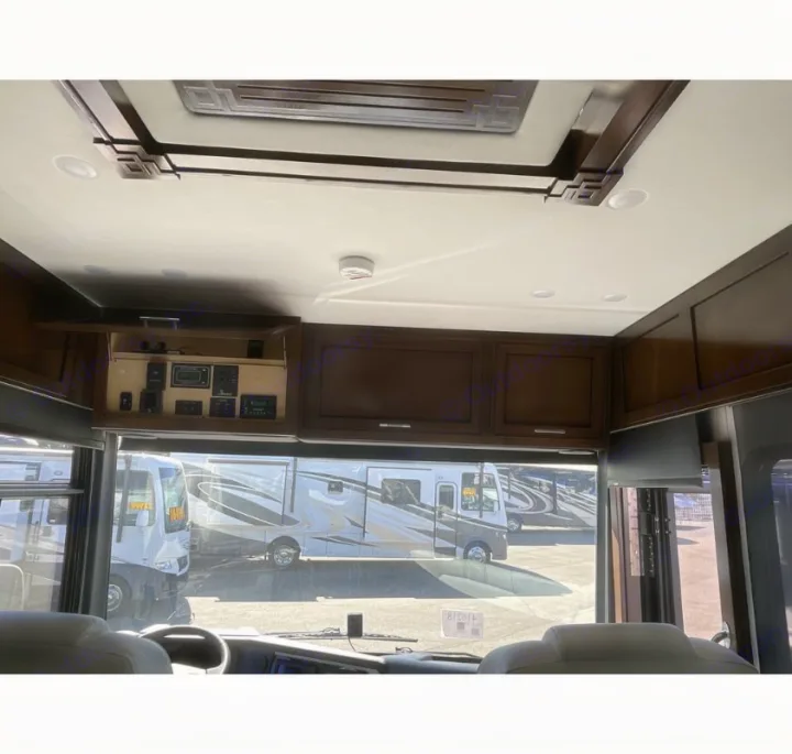 Inside an RV rental: overhead control panel and dark wood cabinets are visible from the driver's seat, with other RVs outside.. Newmar Ventana 2023