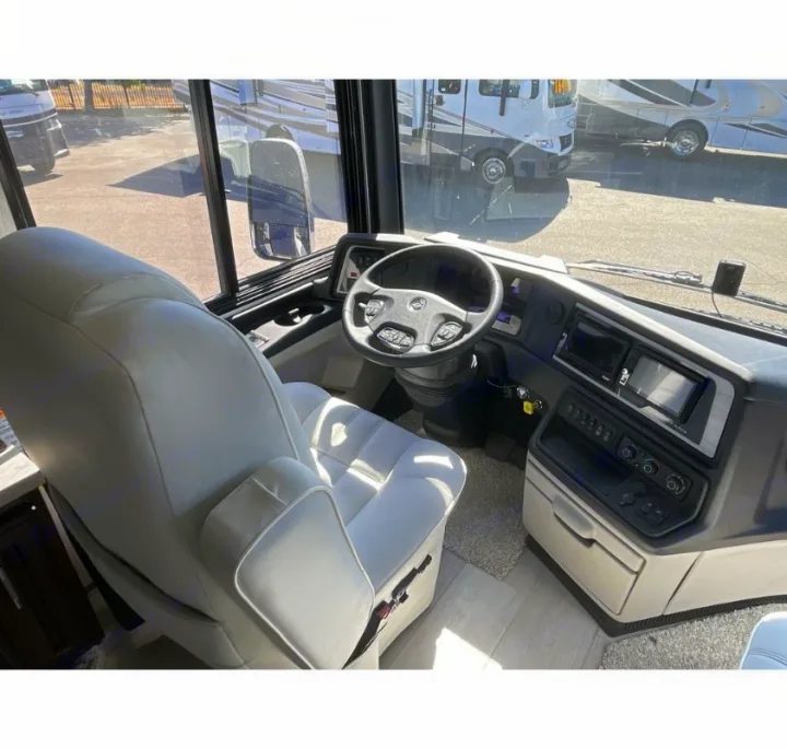RV rental interior: a spacious driver's area with a light-colored captain's seat, steering wheel, and dash screens.. Newmar Ventana 2023