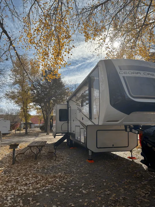 Experience fall camping! This Cedar Creek RV rental is set up under vibrant autumn trees at a sunny campsite.. Cedar Creek Cedar Creek Fifth Wheel 2022