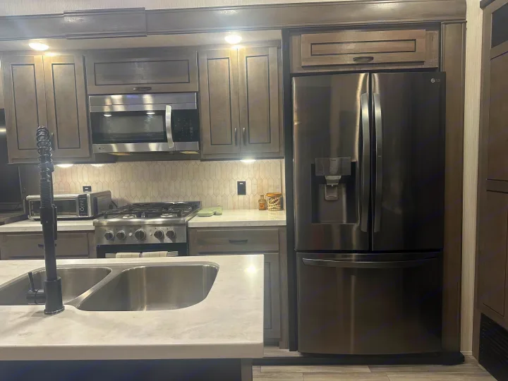 Spacious RV rental kitchen with stainless steel appliances, modern cabinets, double sink, and LG refrigerator.. Cedar Creek Cedar Creek Fifth Wheel 2022