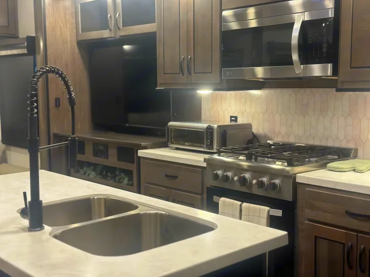 Explore this modern RV rental kitchen, featuring a full oven, microwave, toaster, and double sink for comfortable living on the road.. Cedar Creek Cedar Creek Fifth Wheel 2022