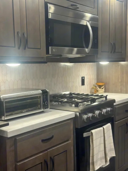 Stylish RV rental kitchen: grey cabinets, stainless microwave, gas stove, Ninja toaster oven, and light patterned backsplash.. Cedar Creek Cedar Creek Fifth Wheel 2022
