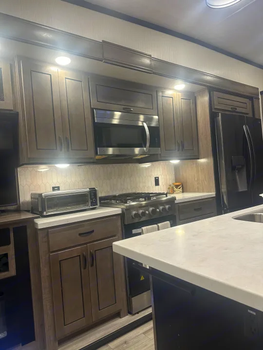 Spacious, modern RV rental kitchen with dark cabinets, light countertops, and stainless steel appliances like a fridge, oven, & microwave.. Cedar Creek Cedar Creek Fifth Wheel 2022