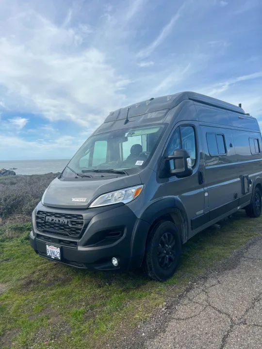 Gray Winnebago Ram rv rental van by the ocean, parked on grass. Perfect for a coastal road trip adventure.. Winnebago Solis BUT59P 2024
