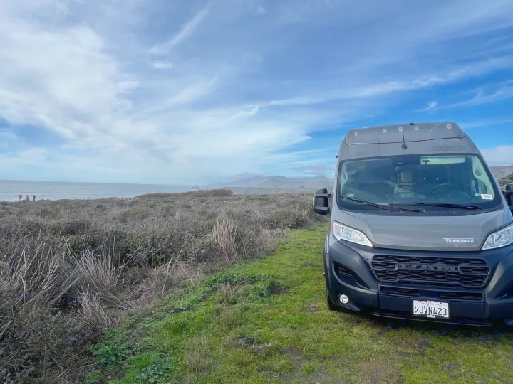 Coastal rv rental trip: A grey Winnebago van is parked on a grassy bluff overlooking the Pacific Ocean and hills.. Winnebago Solis BUT59P 2024