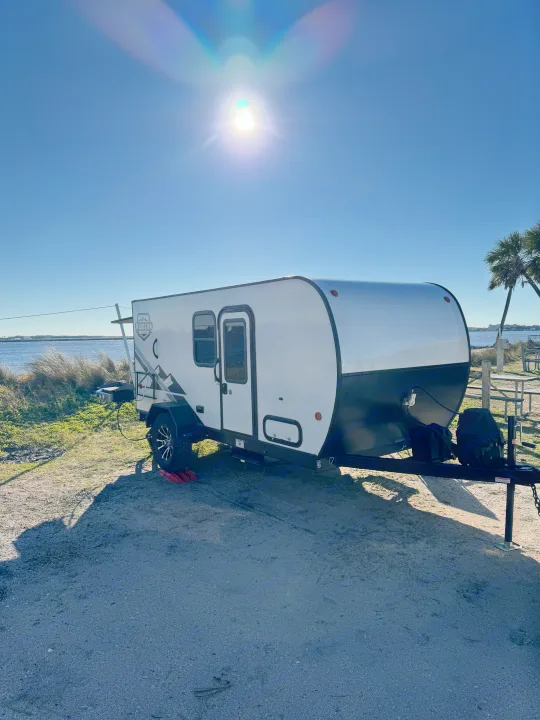 Enjoying a bright day with our RV rental! A modern white travel trailer by the water, parked under a clear blue sky.. Dutchmen Other 2023