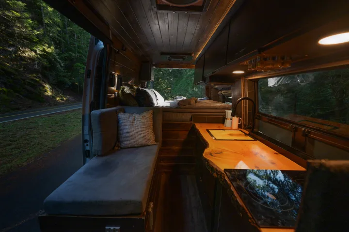 Cozy RV rental interior: bed, living area, live-edge kitchen, & forest views. Perfect campervan tiny home on wheels.. Mercedes-Benz Sprinter 2021