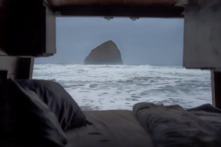 Cozy RV rental view of a majestic sea stack & crashing ocean waves, seen from a comfortable bed inside.. Mercedes-Benz Sprinter 2021