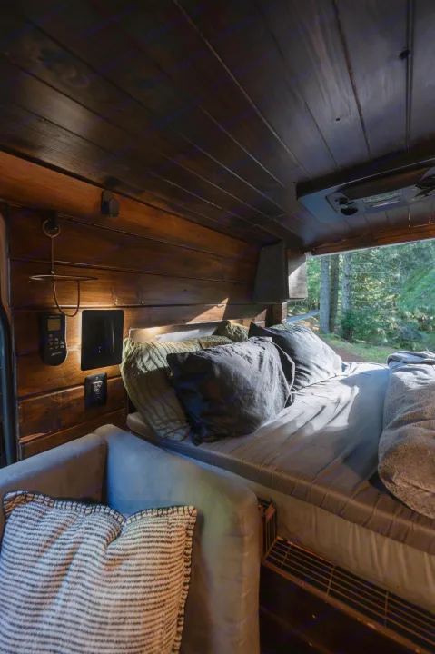 Inviting RV rental interior with a dark wood finish, a cozy bed, and a comfortable seating area, offering a serene forest view.. Mercedes-Benz Sprinter 2021