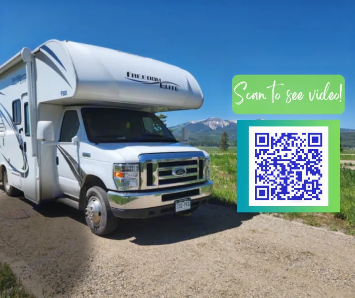 Adventure awaits! A white Class C RV rental is parked on a dirt path with mountains in the background. Scan QR code for video info.. Thor Freedom Elite 2018