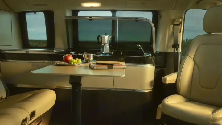 RV rental interior features a cozy kitchen with stove, sink, and dining area with fruit, books, and comfortable seating.. Mercedes Marco Polo Class V 2019