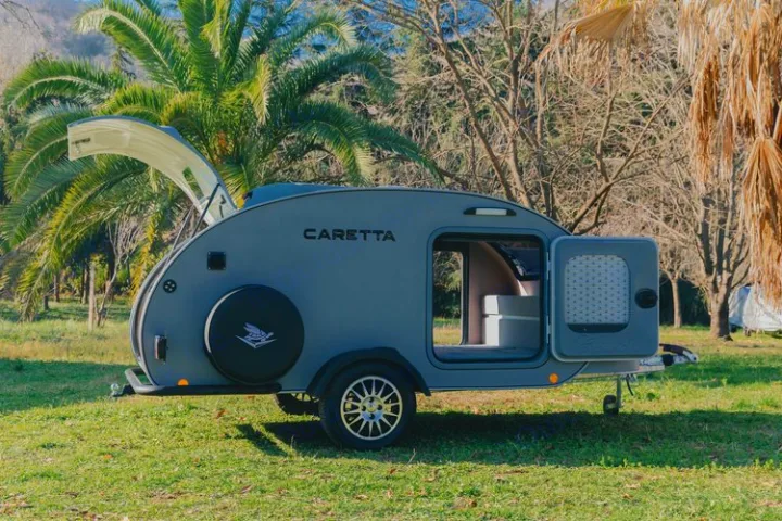 Modern grey teardrop trailer, ideal for **rv rental** adventures. Parked on green grass with trees; hatch & side door open.. Caretta 1500 2024