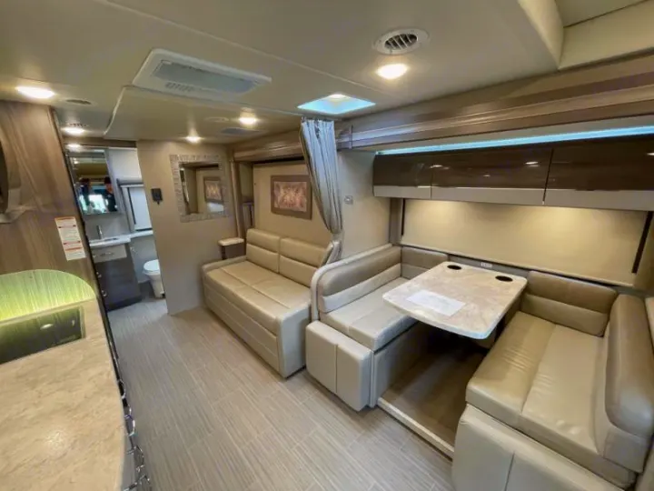 Bright, modern RV rental interior featuring a dinette, sofa, kitchen, and bathroom access. Ideal for motorhome travel.. Thor Delano 2021