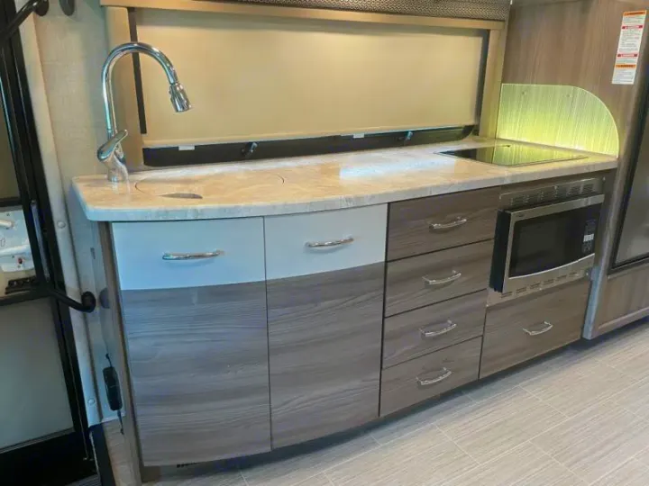 This RV rental features a compact, modern kitchen with a sink, microwave, stove, and ample storage.. Thor Delano 2021