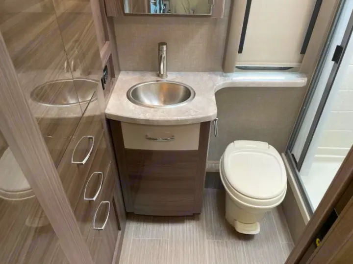Modern, compact RV rental bathroom with stainless steel sink, vanity, toilet, and shower stall, perfect for travel.. Thor Delano 2021