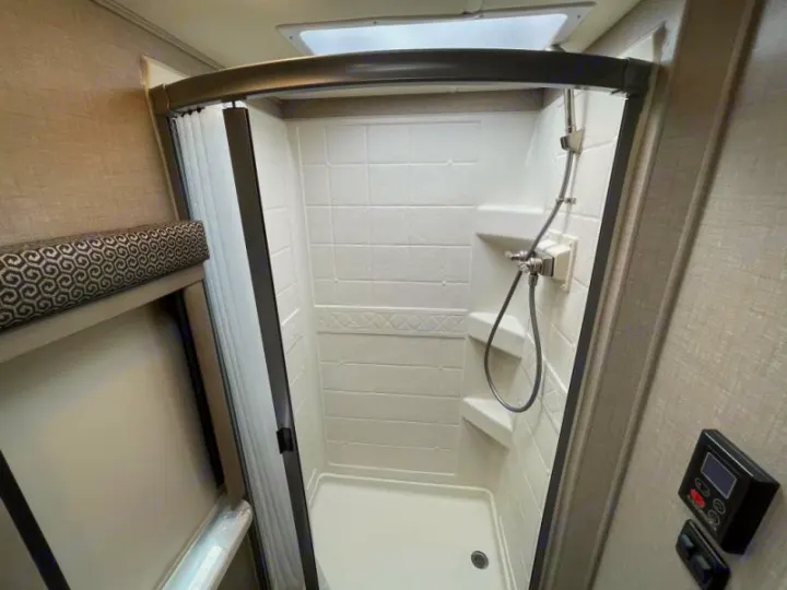 This RV rental offers a compact shower stall with white walls, a flexible showerhead, and nearby digital controls for comfort.. Thor Delano 2021