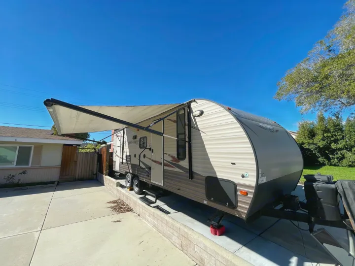 A travel trailer with its awning extended is parked on a sunny driveway, ideal for your next rv rental adventure.. Forest River Cherokee Grey Wolf 2017