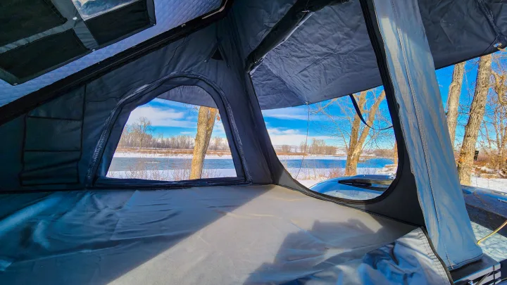 Cozy rv rental rooftop tent interior, featuring a mattress and windows overlooking a snowy river scene.. Toyota Highlander 2003