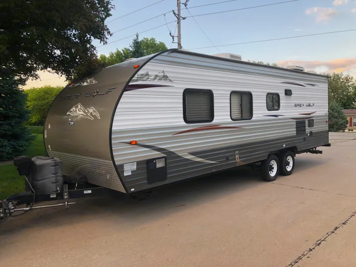 A sleek Grey Wolf RV is parked on a paved driveway, featuring multiple windows and a front hitch area. Great for an rv rental adventure!. Forest River Cherokee Grey Wolf 2013