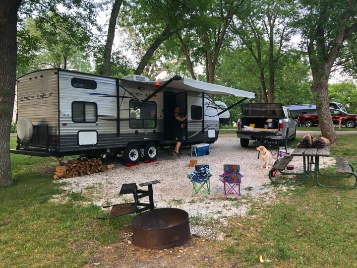 An RV rental, a Grey Wolf travel trailer, is set up at a shaded campsite with a person, dog, and camping gear.. Forest River Cherokee Grey Wolf 2013