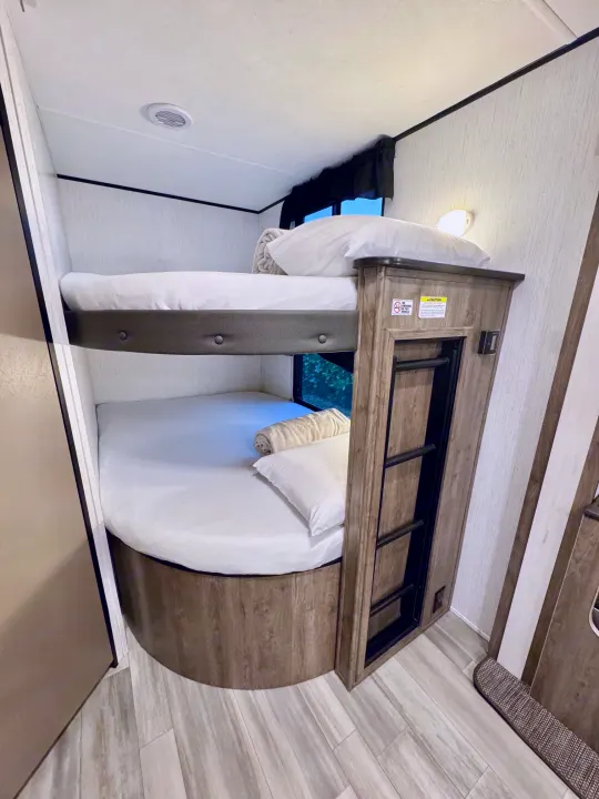 RV rental bunk beds. Cozy interior with white bedding, a ladder, and "NO SMOKING" sign. Ideal for RV trips.. Heartland RVs Pioneer 2021