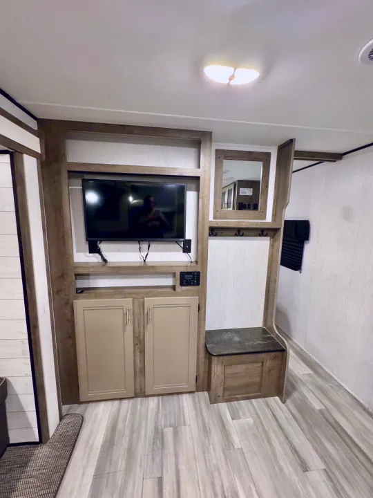 RV rental interior: compact mudroom setup with TV, storage cabinets, mirror, coat hooks, and bench.. Heartland RVs Pioneer 2021