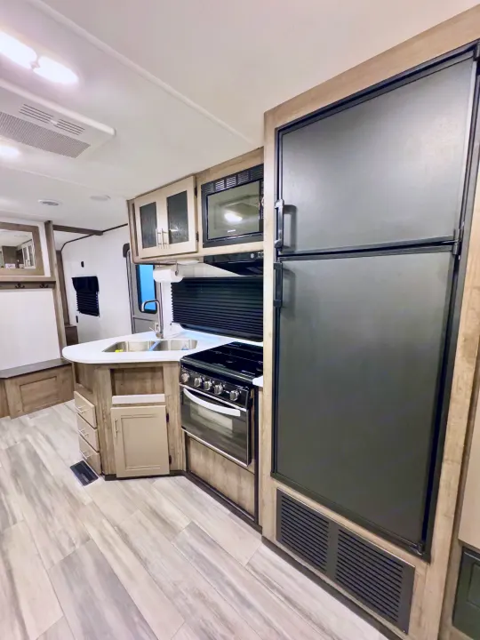 Spacious RV rental kitchen and living area, featuring a modern kitchen with a large fridge, stove, microwave, and sink, plus light wood accents.. Heartland RVs Pioneer 2021