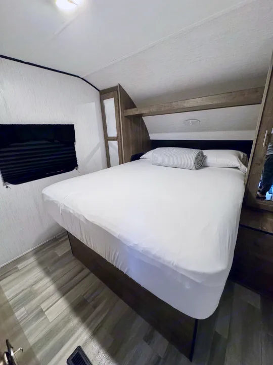 RV rental master bedroom showing a queen bed with white linens and ample built-in storage. Ideal for travelers.. Heartland RVs Pioneer 2021