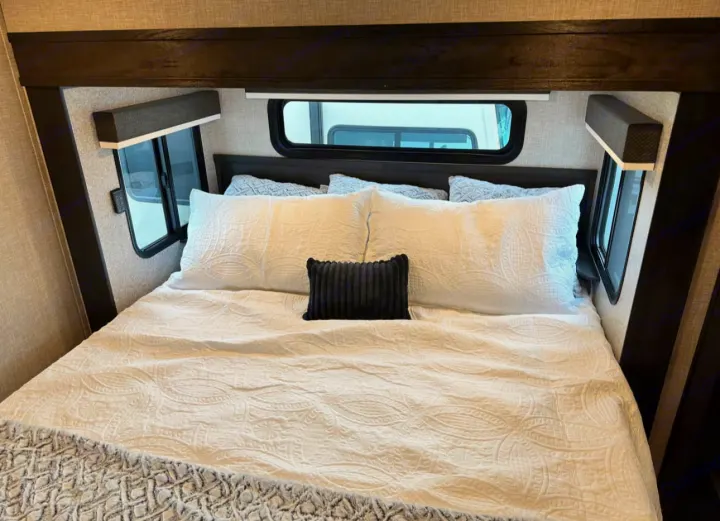 Cozy RV bedroom with comfortable white bedding, perfect for your RV rental getaway. Windows provide natural light.. Jayco North Point 2023