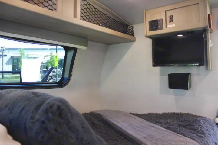 RV rental bedroom interior with TV, overhead storage net, and a window overlooking a street scene.. Forest River GeoPro 2021