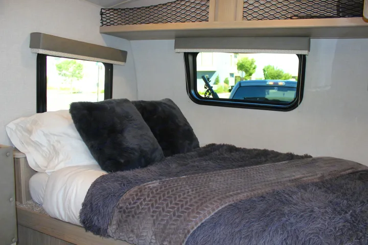 Relax in this RV rental bedroom featuring a cozy bed with fluffy grey blankets and pillows, plus exterior views.. Forest River GeoPro 2021