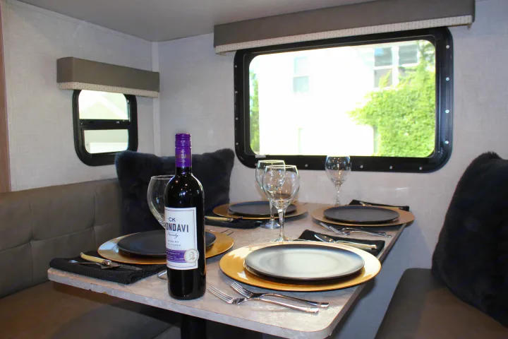 This **RV rental** features a cozy dining area, fully set with plates, wine glasses, and a bottle of wine, perfect for a relaxing meal.. Forest River GeoPro 2021