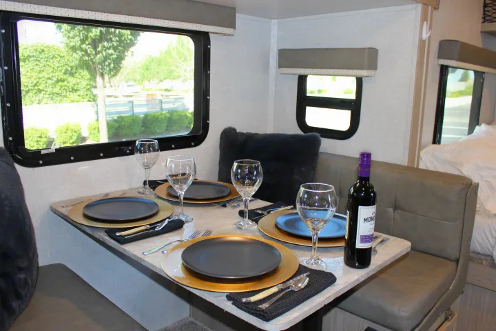 Inside this rv rental: a cozy dinette with a table set for four, wine, and views of nature from the window.. Forest River GeoPro 2021