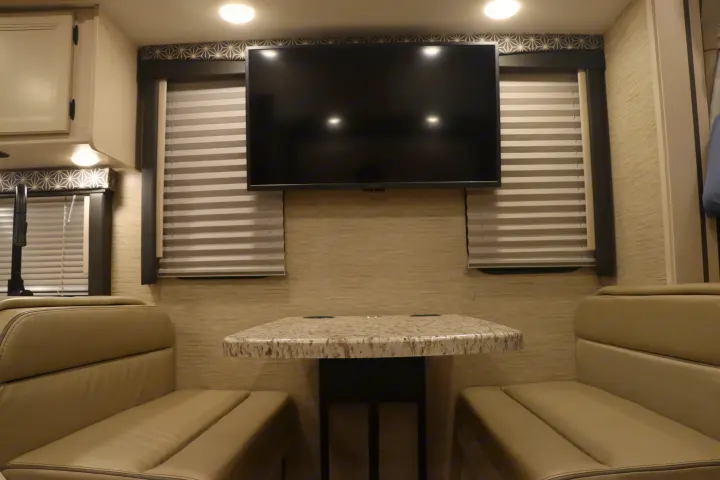Modern RV rental interior featuring a dinette with plush benches, a sleek table, and a wall-mounted TV.. Thor Freedom Elite 2023