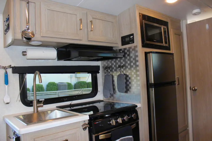 This photo shows a well-appointed rv rental kitchen. It features light wood cabinets, a sink, black stove, microwave, and refrigerator, ideal for travel.. Forest River GeoPro 2021