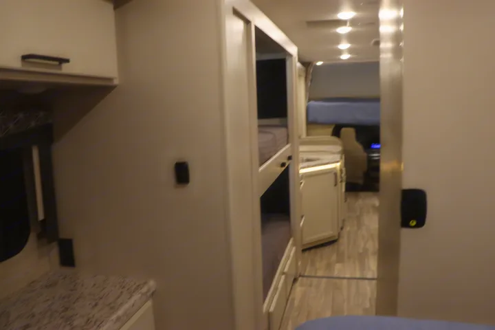 Interior view of an RV rental, featuring bunk beds on the left, overhead cabinets, and a bright hallway leading to the front cab bed.. Thor Freedom Elite 2023