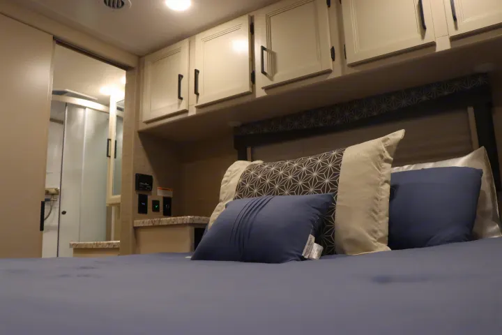 Comfortable RV rental bedroom with modern overhead cabinets, soft bedding, and convenient bathroom access.. Thor Freedom Elite 2023