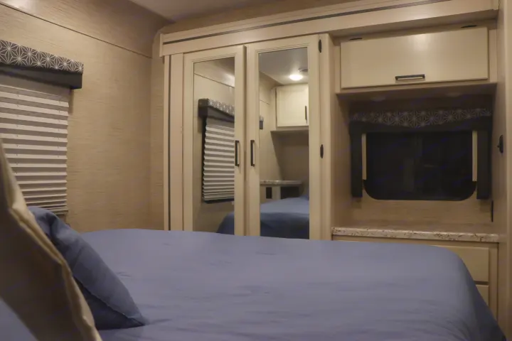 RV rental bedroom with blue bedding, window blinds, and a mirrored wardrobe, offering compact yet functional living space.. Thor Freedom Elite 2023