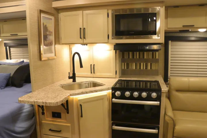 Cozy RV rental: kitchen with sink, microwave, stove; visible bed, and living area in a compact space.. Thor Freedom Elite 2023