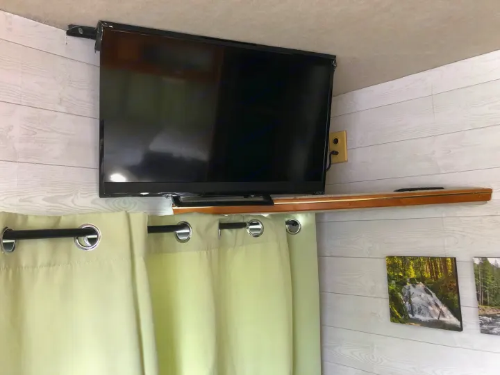 Inside an RV rental: a corner-mounted TV, light green curtains, and a shelf. White shiplap walls with nature art.. Fleetwood Other 2007