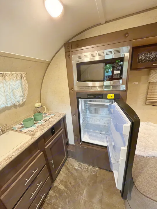 Inside an RV rental: functional kitchen featuring a sink, microwave, and open refrigerator. Ready for your next trip!. R-Pod Hood River Edition 2016