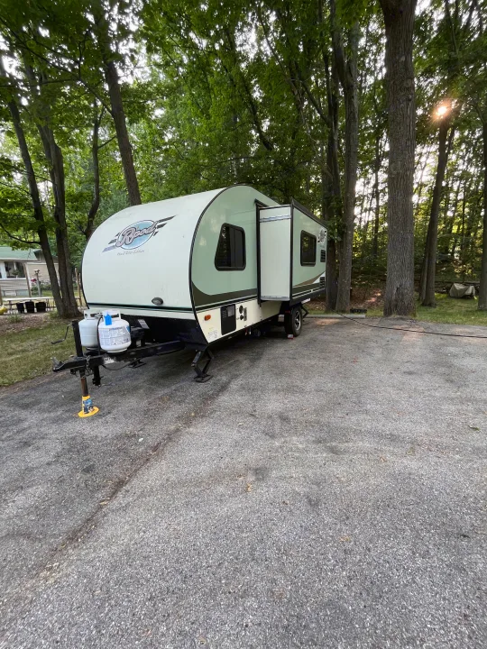 A white and green Rockwood travel trailer, perfect for an **rv rental**, is parked on an asphalt lot in a wooded campground.. R-Pod Hood River Edition 2016