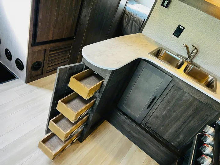 Modern RV rental interior: kitchen with sink, dark cabinets, and clever pull-out storage/stairs. Bedroom visible.. Forest River Coachmen Leprechaun 2023